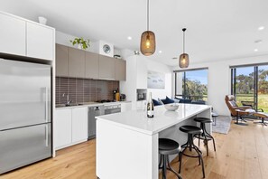 A modern kitchen with a central island, stainless steel appliances, and pendant lighting. - Magic Driftwood (Torquay)