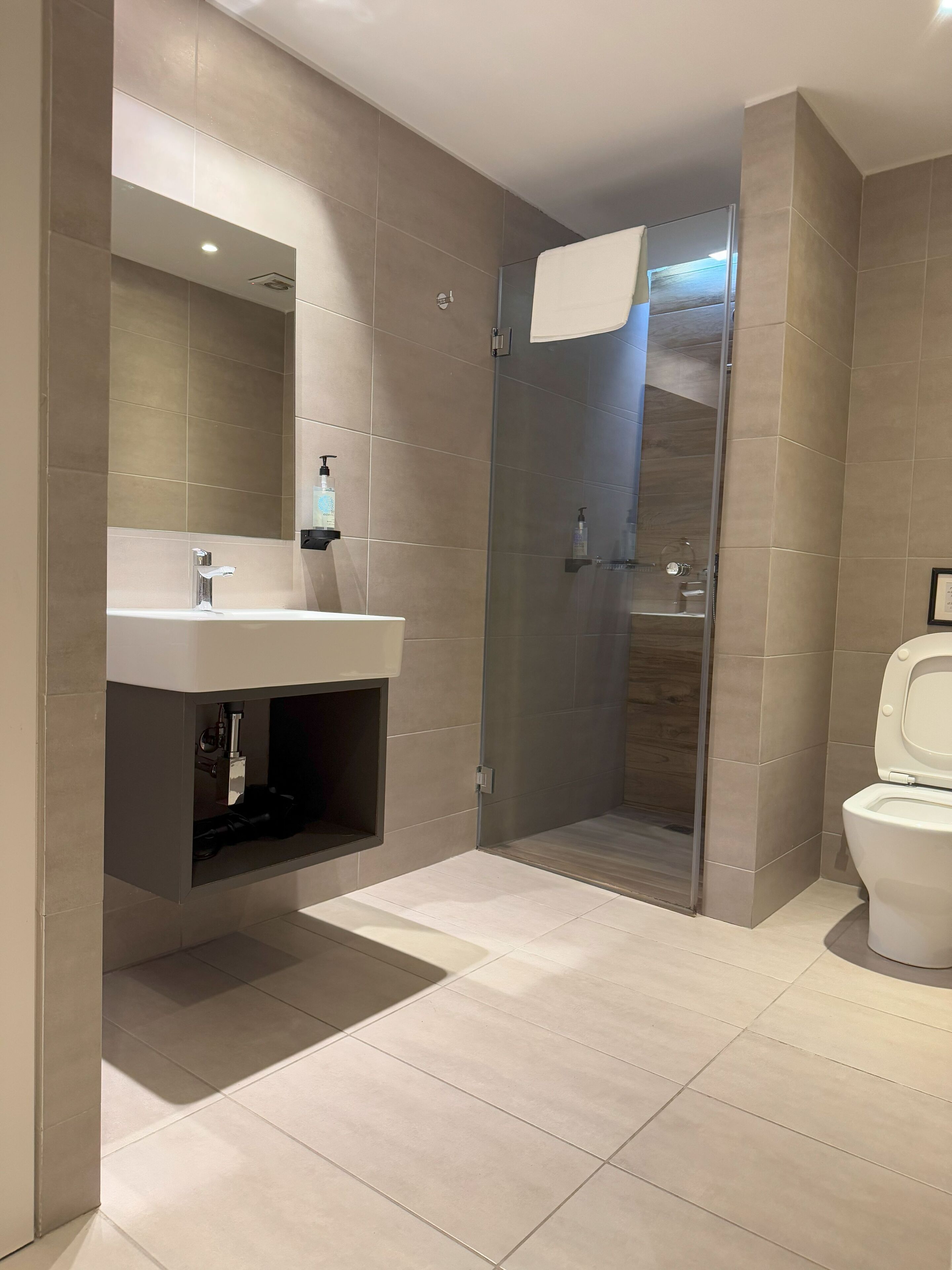 A modern bathroom with a glass-enclosed shower, a white sink with a mirror, and a toilet.