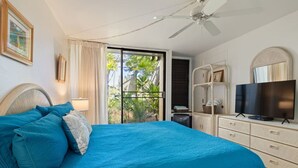 Una camera da letto con un grande letto, una televisione, un ventilatore a soffitto e vista sul verde.