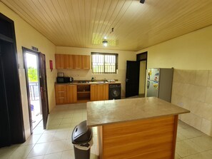 A kitchen with wooden cabinets, a microwave, a sink, a washing machine, and a refrigerator. - The Charways Lodge (Accra)