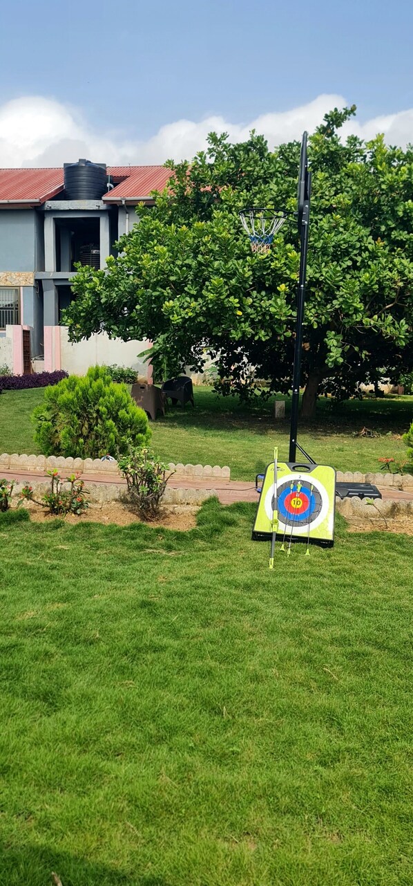 A grassy area with a target board for archery, a tree, and a building with a red roof in the background.