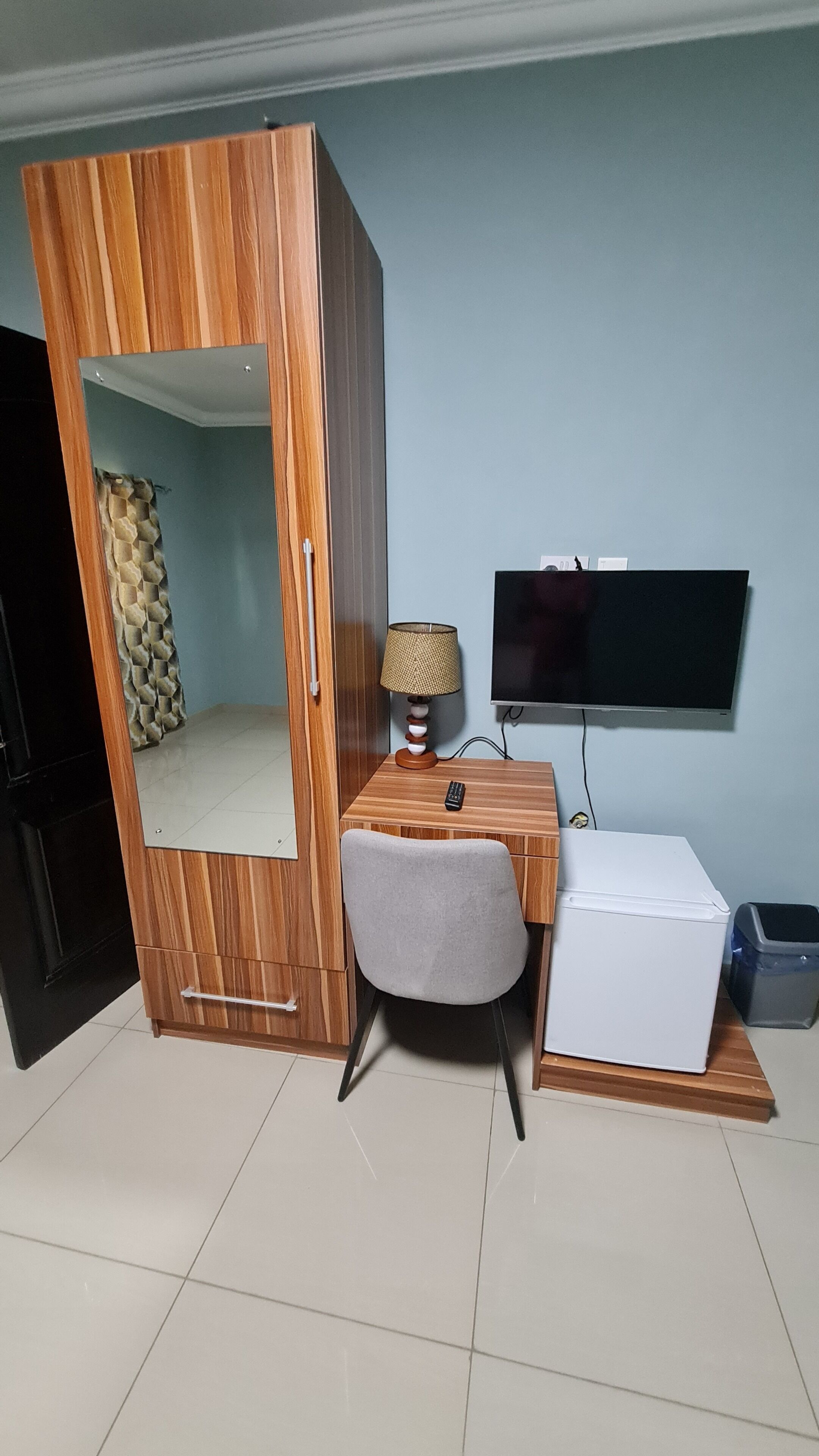A room with a wardrobe, a desk with a chair, a television, and a small white appliance.