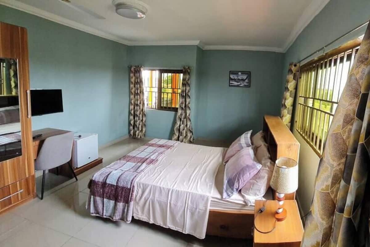 A bedroom with a bed, a desk, a chair, a TV, and curtains.