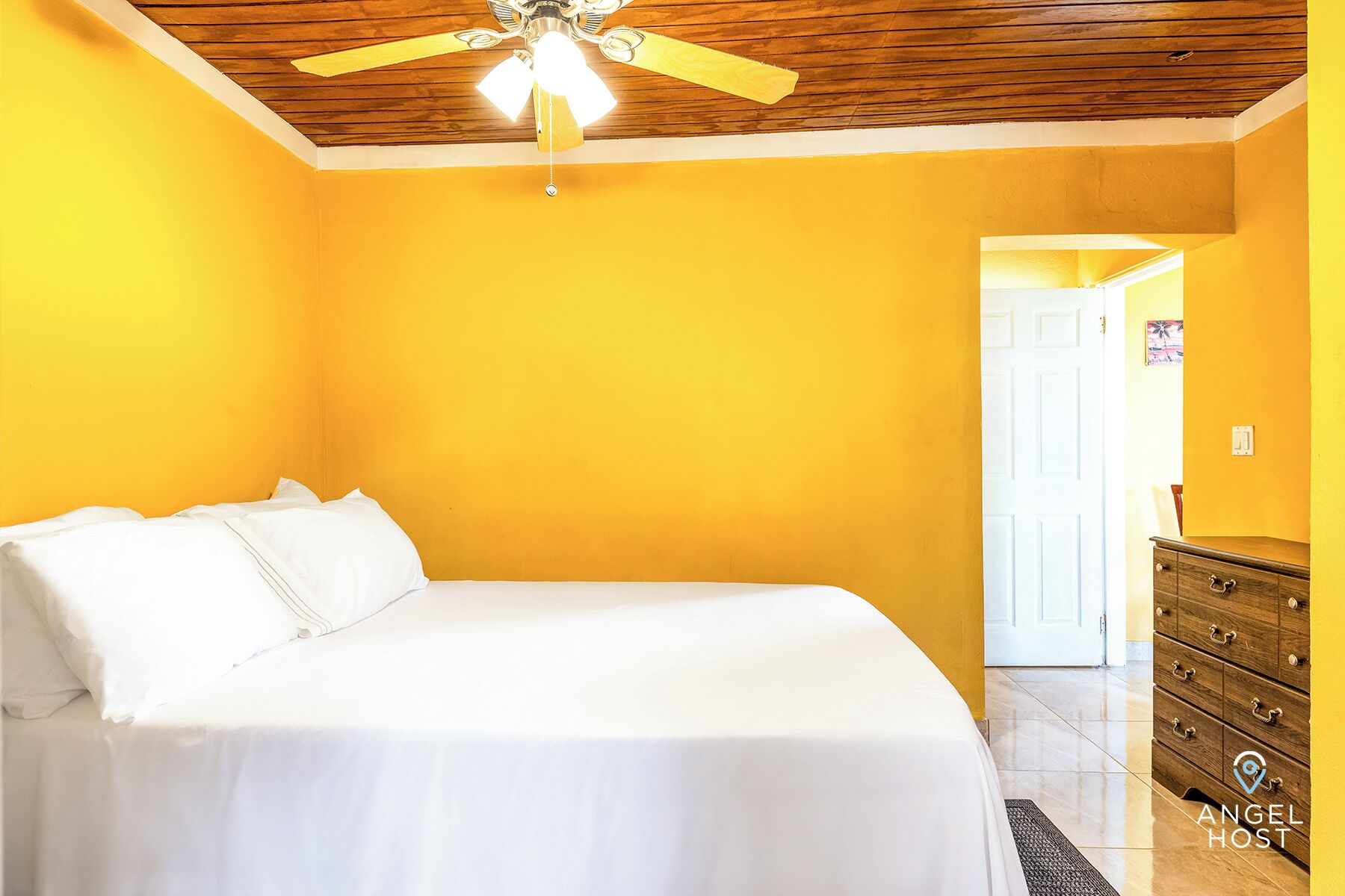 A bedroom with a bed, a wooden ceiling fan, and a dresser.