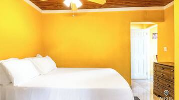 A bedroom with a bed, a wooden ceiling fan, and a dresser.