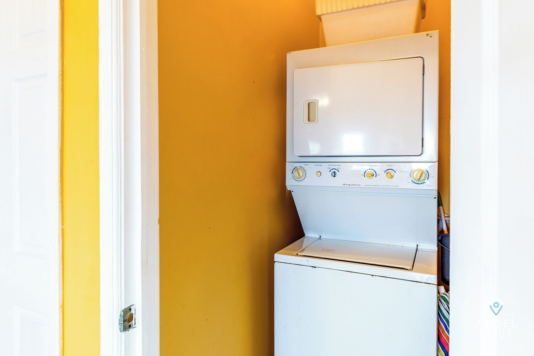 A compact laundry room with a stacked washer and dryer, a door, and a yellow wall.