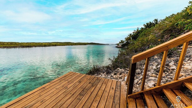 A wooden deck leading to a calm body of water with clear turquoise water, surrounded by greenery and a clear sky. - Chalk Sound Beach Residences (Providenciales)