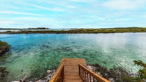 A wooden pier leading into a clear blue body of water with a distant shoreline and vegetation. - Chalk Sound Beach Residences (Providenciales)