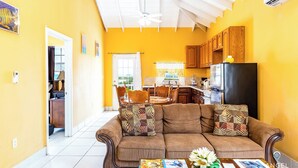 A cozy living room with a sofa, a dining table, and a kitchen area with wooden cabinets and a refrigerator. - Chalk Sound Beach Residences (Providenciales)