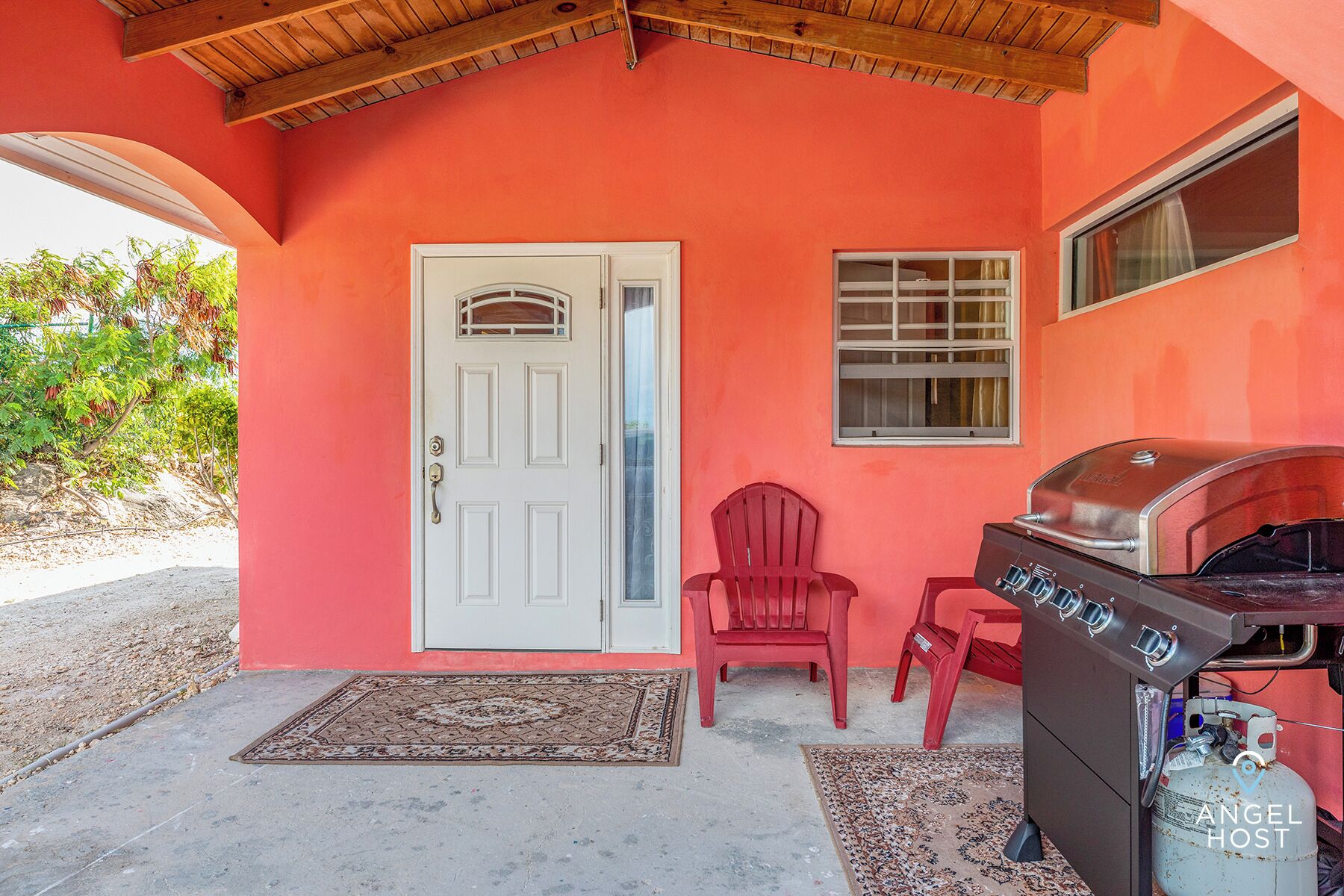 A house with a red exterior, a white door, and a barbecue grill.
