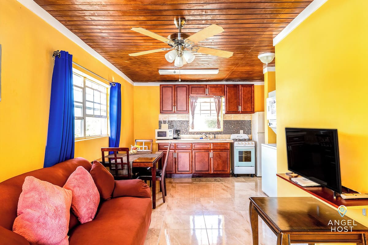 A living room with a brown leather sofa, a wooden ceiling fan, and a television on a wooden table.
