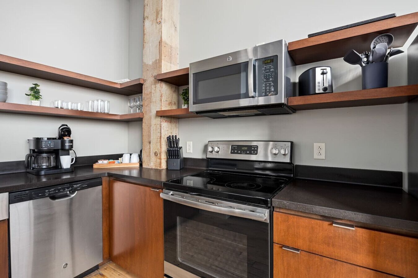 A modern kitchen with stainless steel appliances, wooden shelves, and a coffee maker.