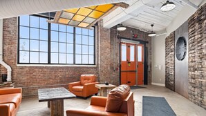 A spacious lobby with brick walls, large windows, and a mix of leather and wooden furniture. - Cooperage 214 | Mid-century 1BD Loft | Peoria (Peoria)
