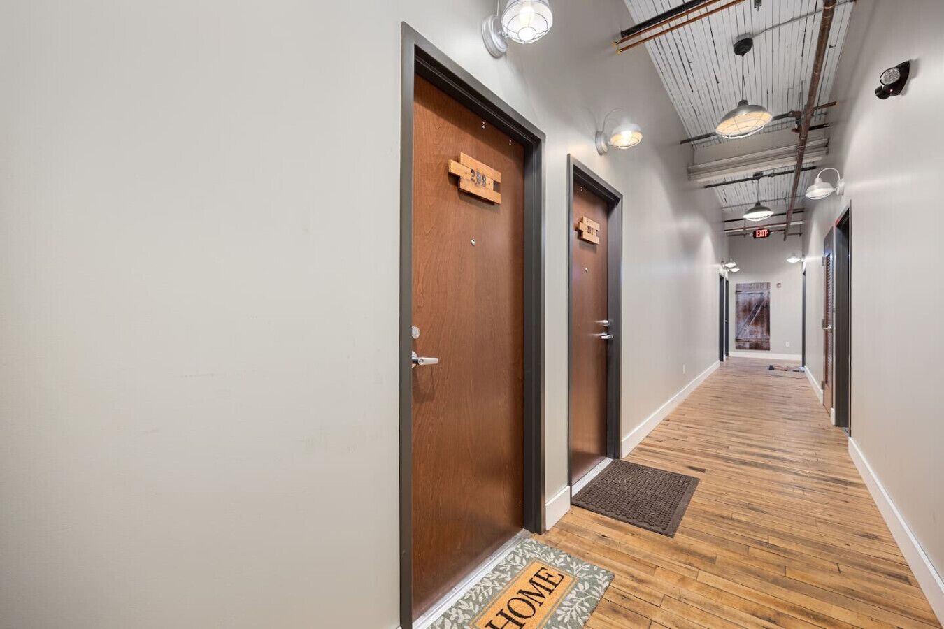 A hallway with wooden doors, a welcome mat, and a ceiling with exposed beams and lighting fixtures.