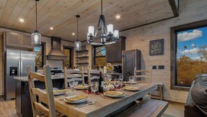 A modern kitchen with a wooden table set for dining, stainless steel appliances, and a large window with a view of trees.