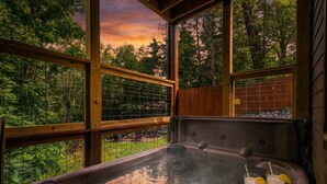A hot tub with a glass table, two drinks, and a view of trees through large windows.