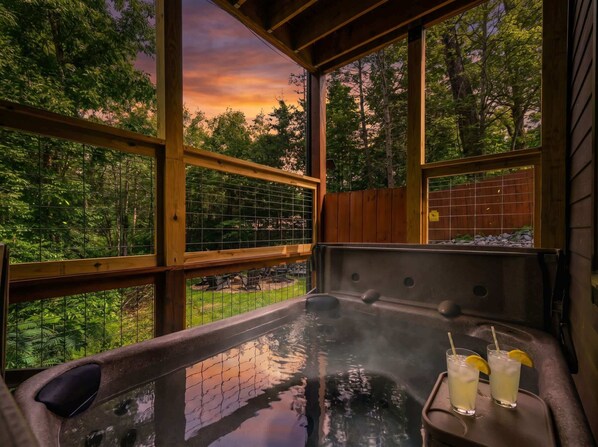 A hot tub with a glass table, two drinks, and a view of trees through large windows.