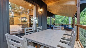 A wooden deck with a table and chairs, a sofa, and a bed visible through a glass wall.