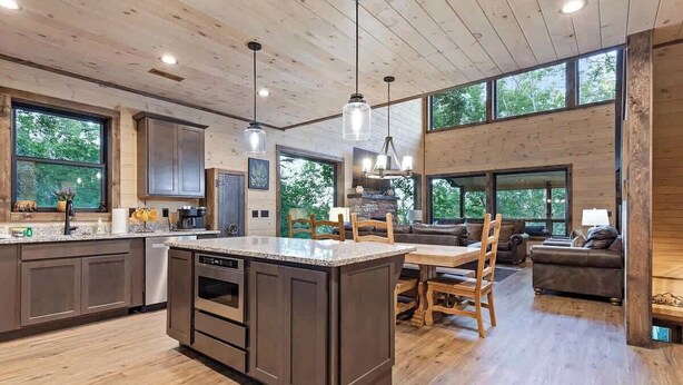 A spacious kitchen with a central island, wooden cabinets, and large windows offering views of the outdoors.