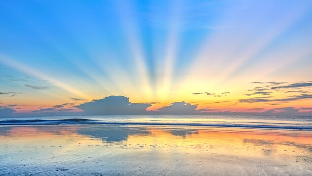 A beach with a sunset and calm waves.