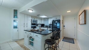 A modern kitchen with white cabinetry, a central island with stools, a refrigerator, and a microwave.