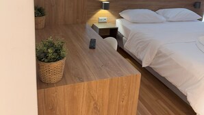 Een moderne slaapkamer met een houten hoofdeinde, een nachtkastje met een lamp, een afstandsbediening en twee potplanten.
