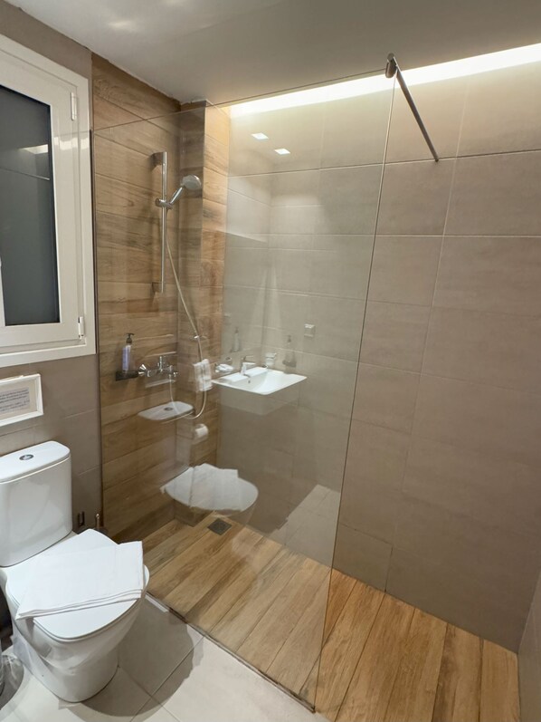 A modern bathroom with a glass-enclosed shower, a white toilet, and a wooden vanity.