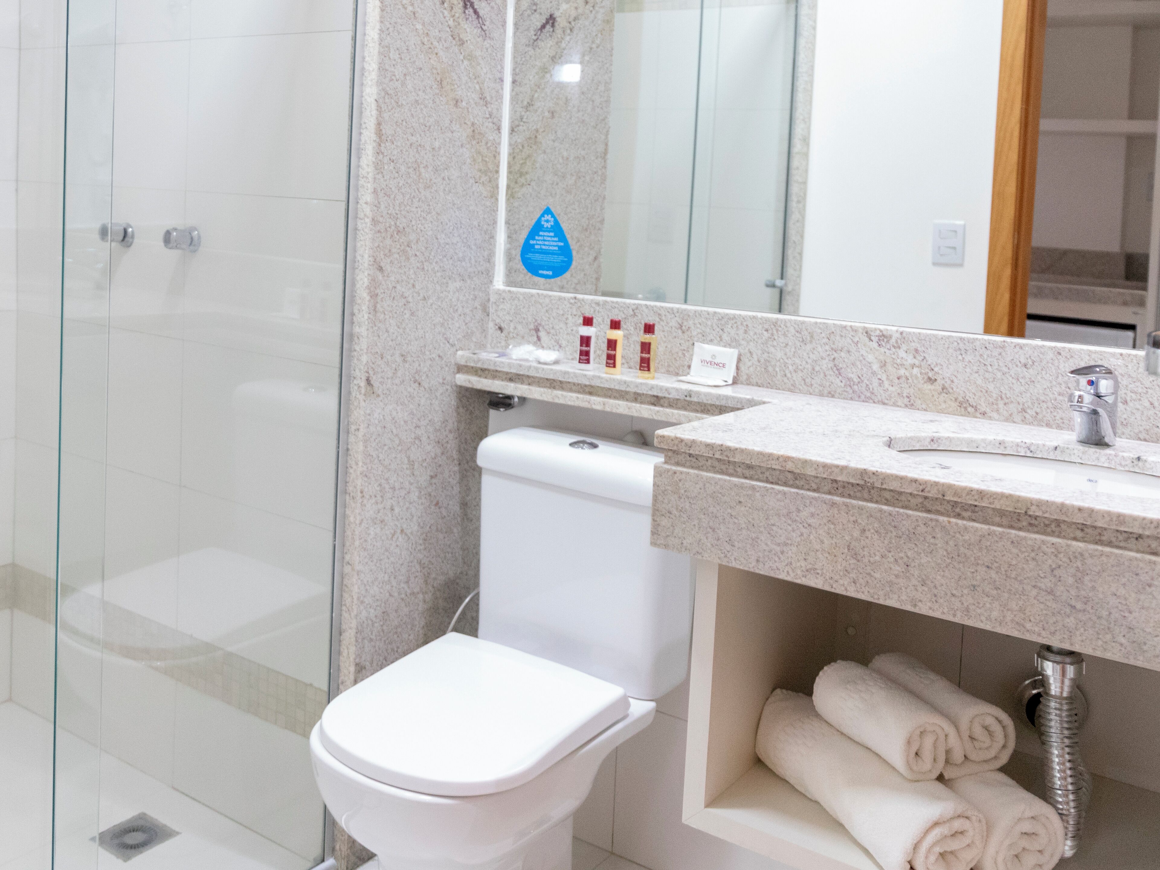 A modern bathroom with a glass shower enclosure, a white toilet, a marble countertop, and a sink with a mirror above.