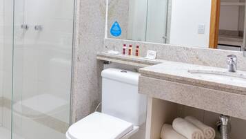 A modern bathroom with a glass shower enclosure, a white toilet, a marble countertop, and a sink with a mirror above.