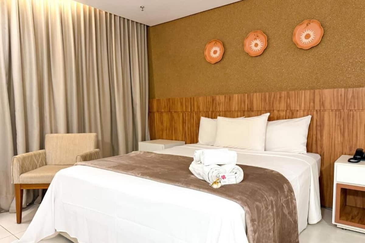 A hotel room with a bed, a chair, a nightstand, and a wall with decorative plates.