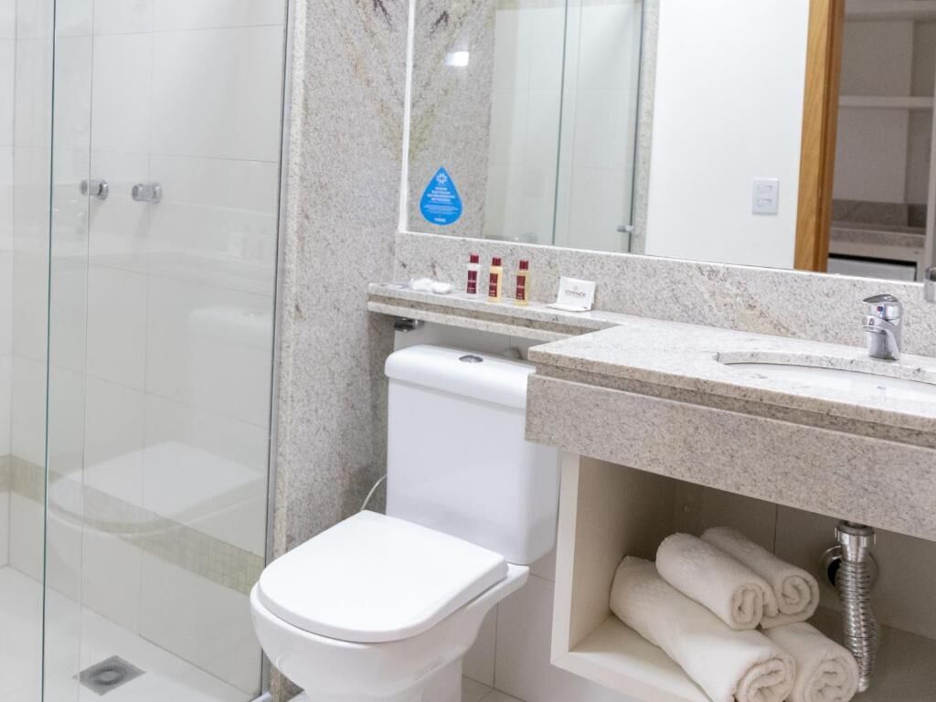 Ein modernes Badezimmer mit Duschkabine aus Glas, einer weißen Toilette, einer Marmorarbeitsplatte und ordentlich aufgerollten Handtüchern.