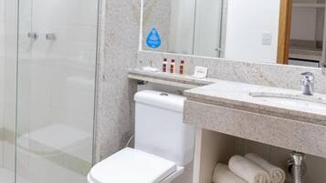 A modern bathroom with a glass shower enclosure, a white toilet, a marble countertop, and neatly rolled towels.