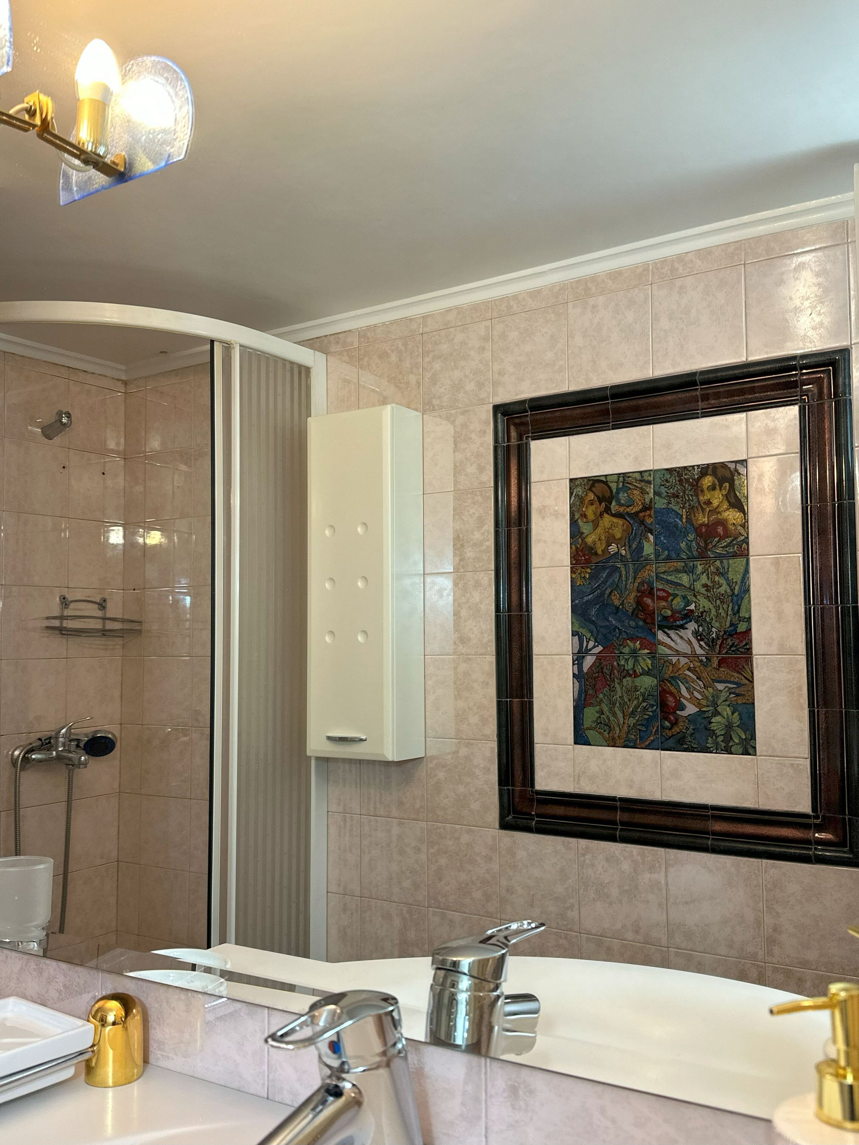 A modern bathroom with a shower, a sink with a gold faucet, and a framed tile artwork on the wall.
