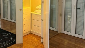 A room with a walk-in closet, a bed with white bedding, and a ceiling-mounted air conditioning unit. - Acropolis Elegant Apartment II (Athina)