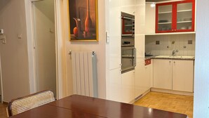 A modern kitchen with white cabinets, red accents, and a painting above the counter. - Acropolis Elegant Apartment II (Athina)