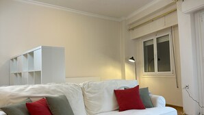 A white sofa with red and grey cushions, a black coffee table, and a white shelving unit against a wall with a window. - Acropolis Elegant Apartment II (Athina)