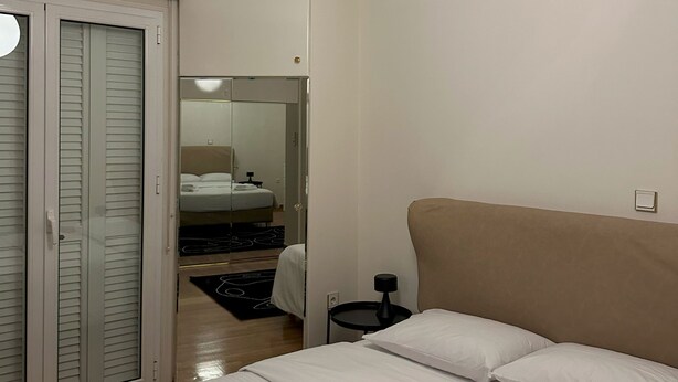 A bedroom with a bed, a bedside table, a lamp, a wardrobe, and a mirror. - Acropolis Elegant Apartment II (Athina)