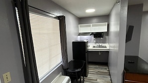A compact kitchenette with a built-in stove, a sink, and a window with blinds.