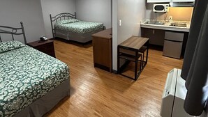 A compact room with two beds, a small kitchenette, and a wooden floor.