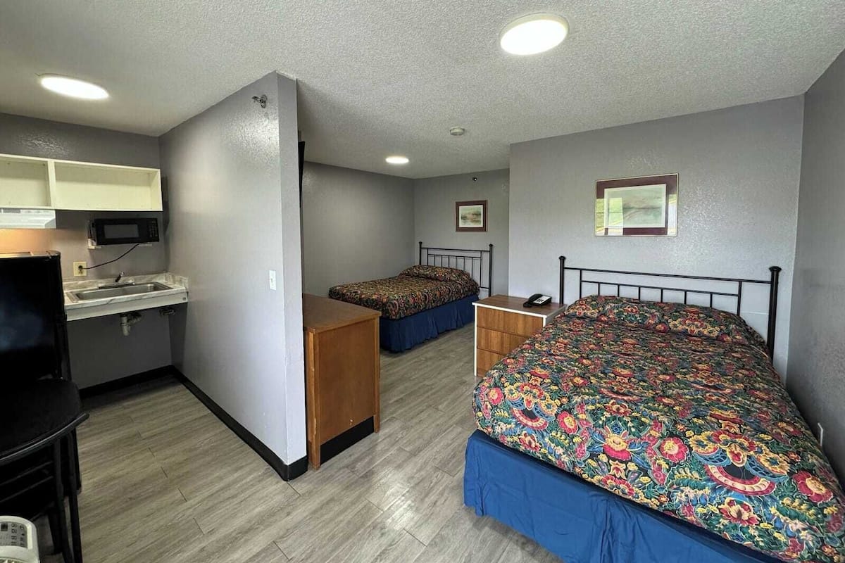Una habitación compacta con kitchenette, una cama con colcha floral colorida y un escritorio pequeño.