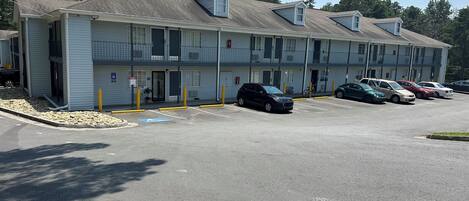 A motel with multiple parking spaces, a covered parking area, and a building with a flat roof and dormer windows.