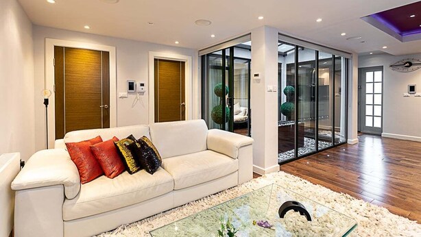 Un salon moderne avec un canapé blanc, une table basse en verre et une porte vitrée donnant sur un balcon.