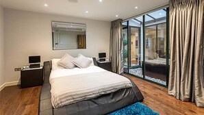 Une chambre moderne avec un grand lit, une table de chevet, un miroir et une porte-fenêtre coulissante donnant sur un balcon.