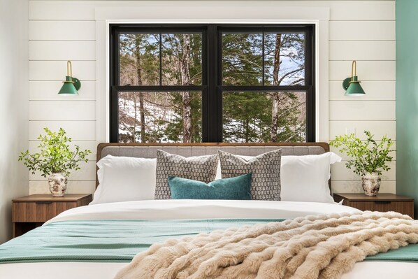 A bedroom with a large window, two bedside tables with lamps, a bed with patterned pillows, and a view of trees outside. - Heated POOL|Views|HotTub|Sauna|2mi to SR Golf Club (Bethel)