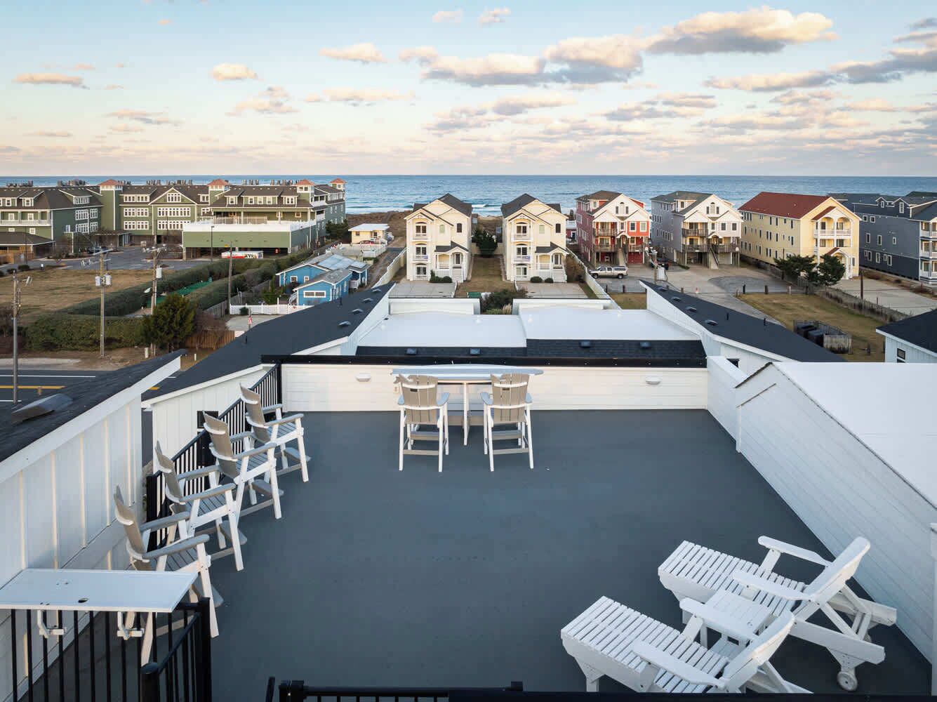 Una terrazza sul tetto con sedie e tavoli bianchi, con vista su una zona costiera con case e il mare.