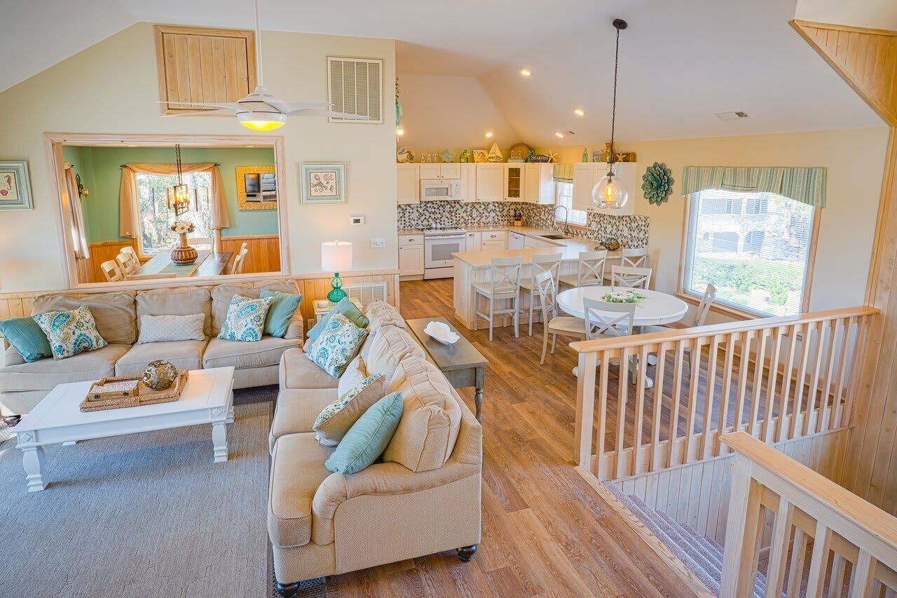 A spacious living area with a sofa set, dining table, and kitchen in the background.