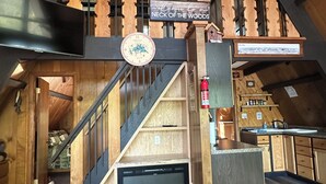 Un intérieur en bois avec un escalier, une pancarte de bienvenue, une horloge et un extincteur.