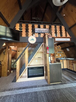 A wooden interior with a staircase, a welcome sign, a clock, and a fire extinguisher.