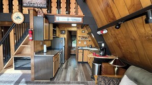 L’intérieur chaleureux d’un chalet, avec un revêtement mural en bois, un coin cuisine, un espace repas et un escalier.