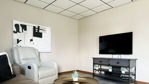 Een moderne woonkamer met een leren bank, een witte fauteuil, een ronde salontafel, een flatscreen televisie en een donker houten dressoir.